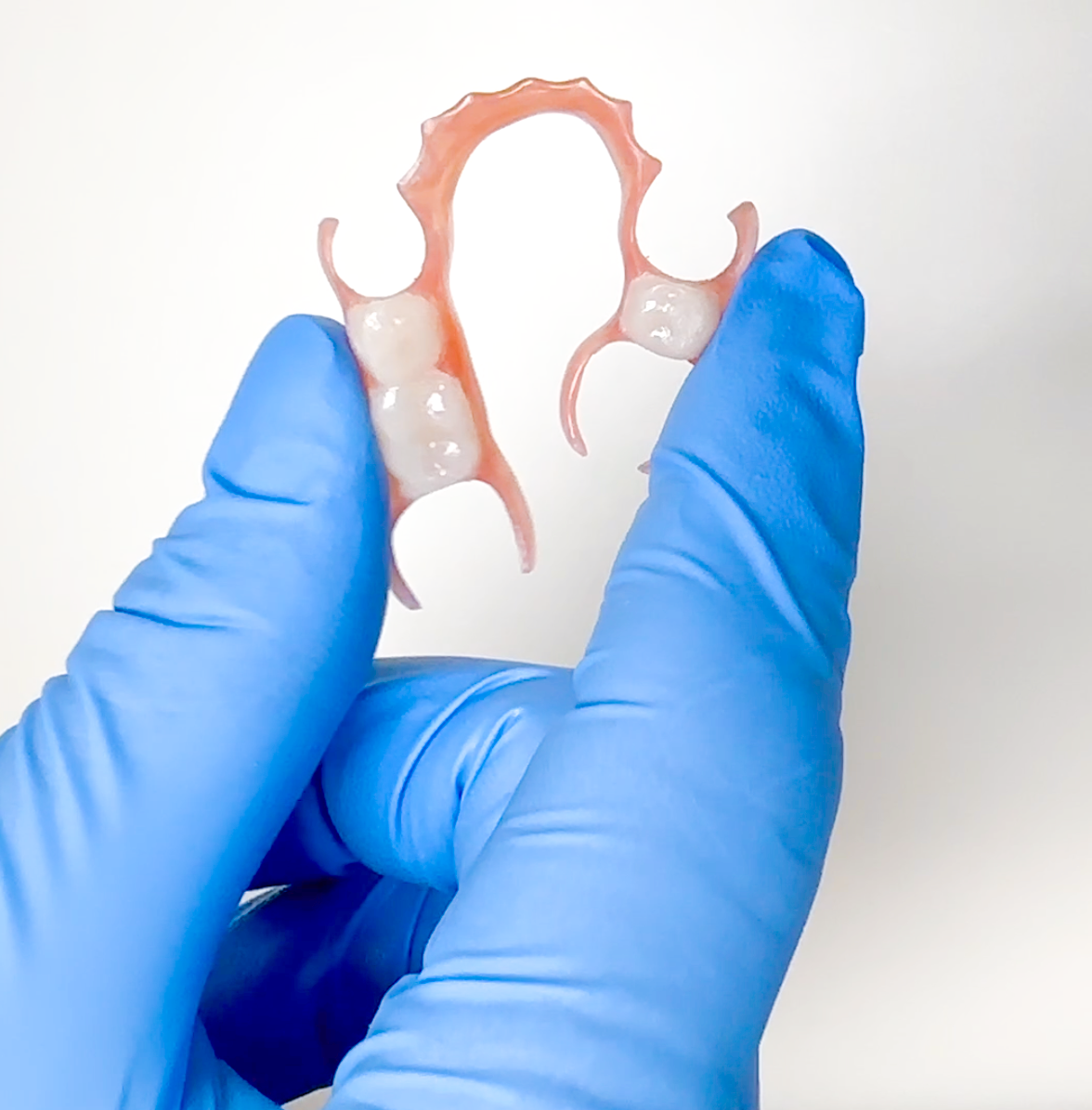 Flexible partial denture held by a person wearing blue gloves on a white background